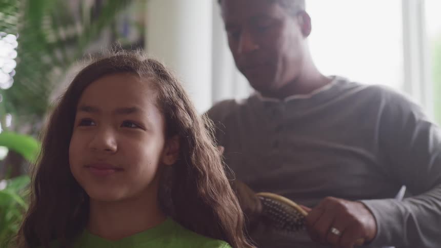 Father combs his daughters hair in the living room at home
