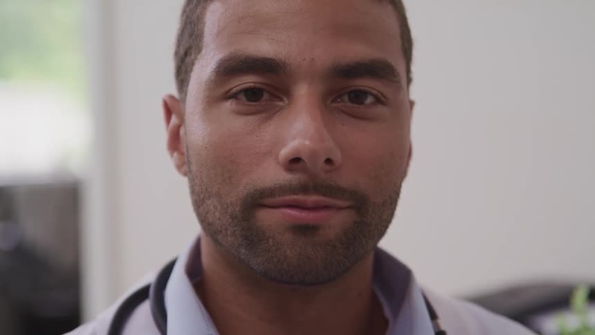 A man in a room with a lab coat and a stethoscope with a wall in the background