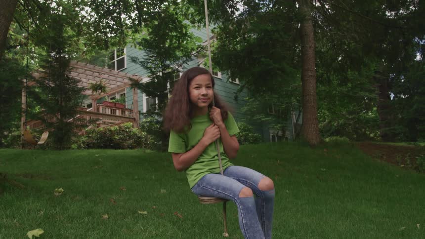 Girl sitting in a swing hanging from a tree in the backyard at home
