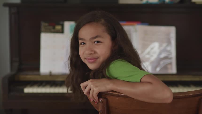 A girl sits by the piano smiling