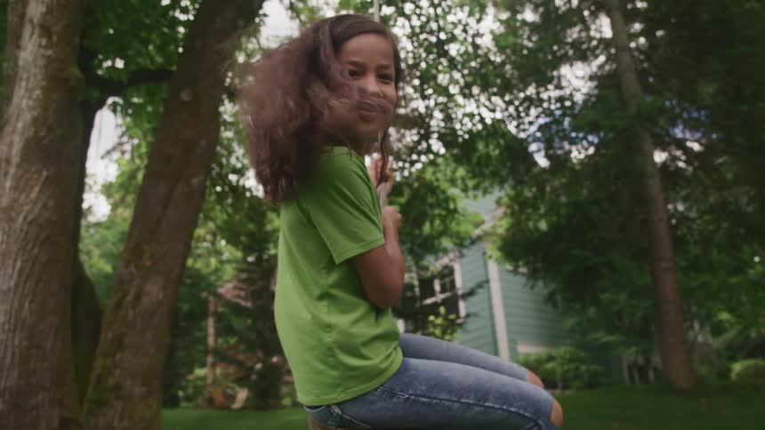A young girl playing on a tree swing in a yard at home