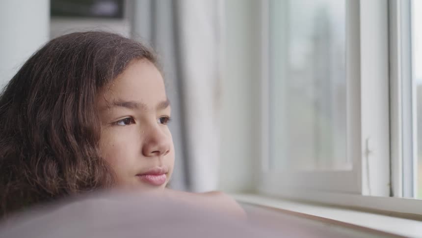 Young girl looking pensively out the window