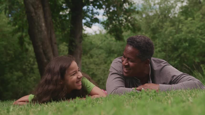 Father and daughter talking and laughing laying in the grass outdoors