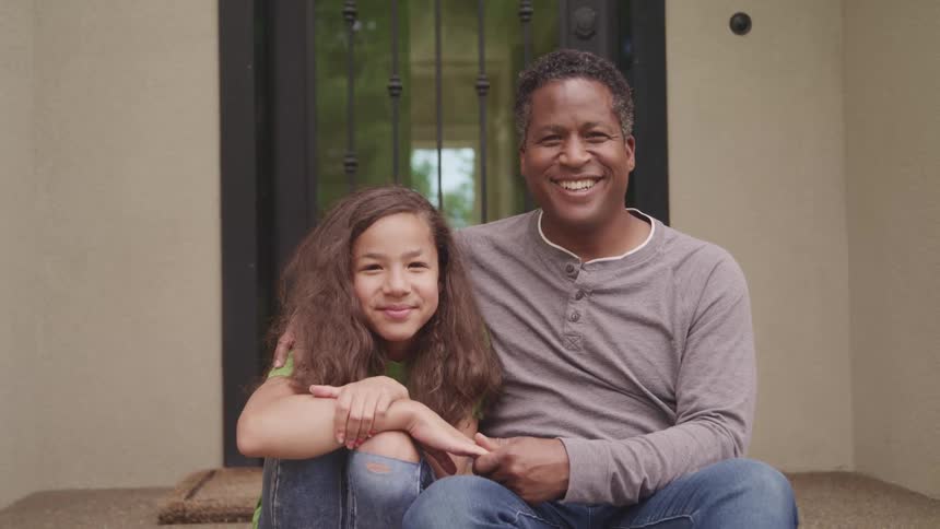 A man and a girl sitting on a porch with a wall and a door in the background