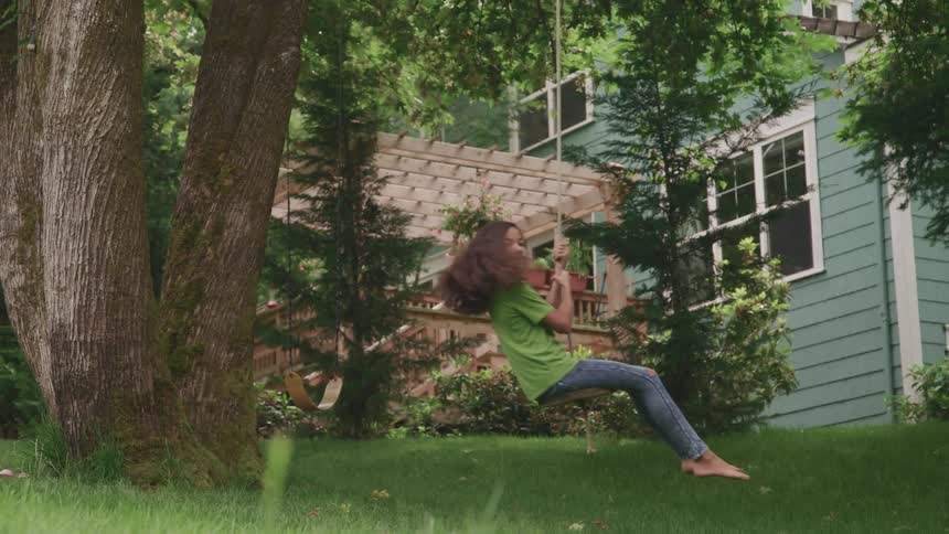 A girl playing on a tree swing in a yard on a summer day