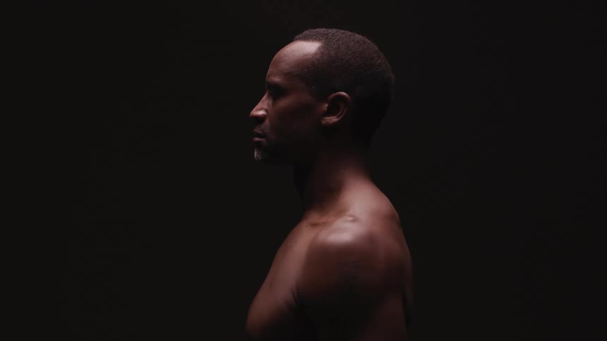 A man stands shirtless in a dark room