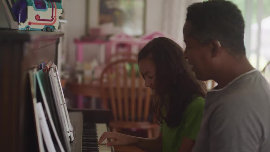 A father and teenage daughter playing piano together at home