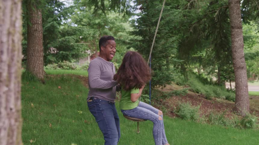 A father pushing his daughter on a swing outdoors