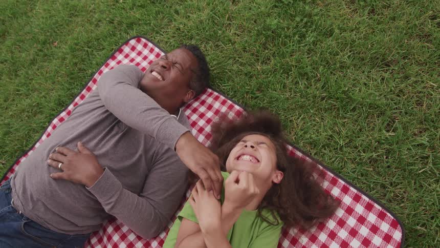 Father and daughter tickling each other over a blanket on the grass