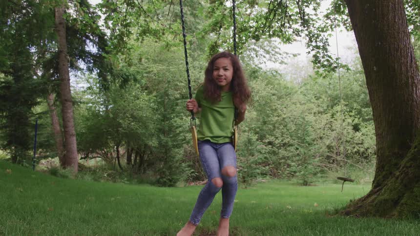 A young girl sitting on a swing hung from a large tree