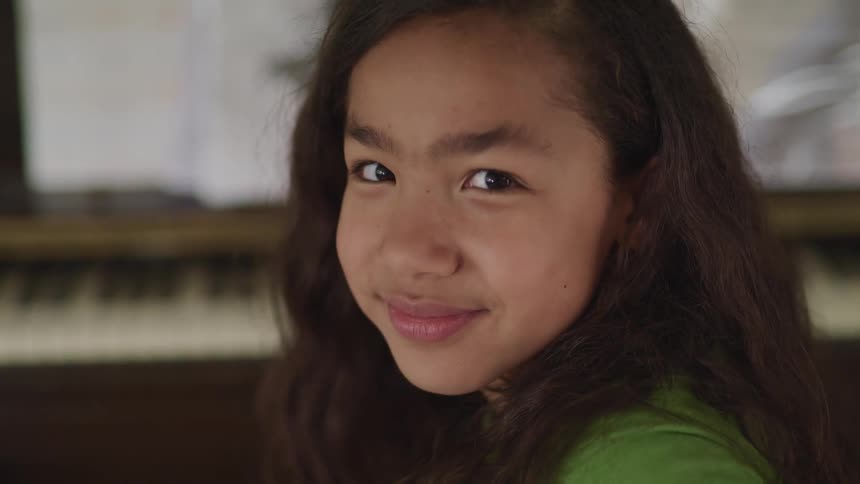 A girl in a room staring with a piano in the background