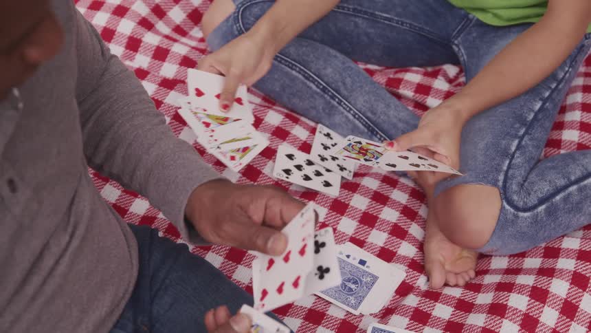 A man and a girl sitting on a blanket playing cards