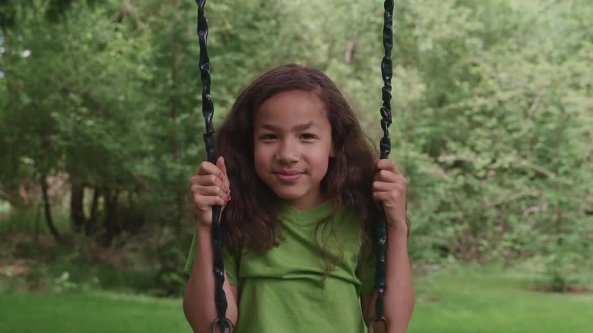 A young girl sitting on a playground swing on a summer day