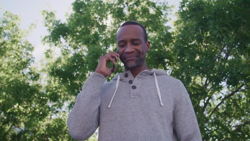 A man smiles and nods his head while speaking on a smartphone outdoors on a sunny day