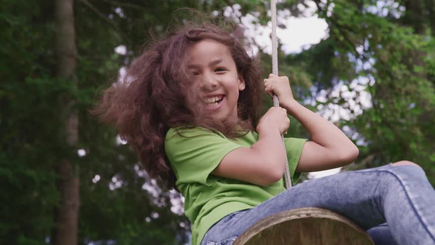 Happy child swinging on a rope swing pushed by her father