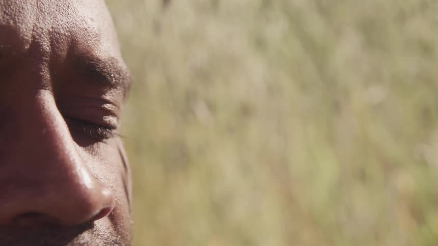 A man stands in a grassy field with the sun shining down on him and closes his eyes