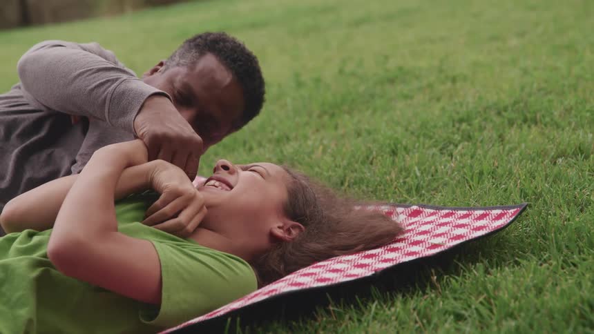 A man and a girl laying on a blanket on grass