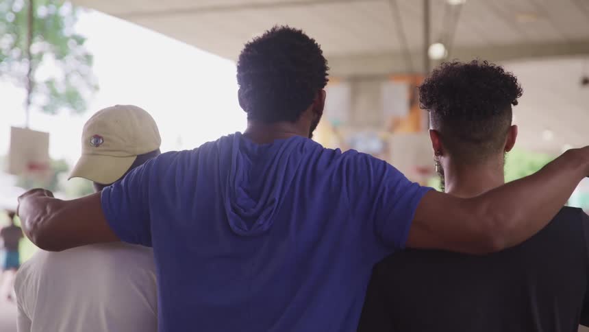 A man standing in the middle reaches out and puts his arms around the shoulders of his brothers