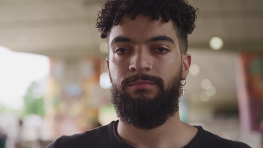 A black man looks straight ahead while people move around behind him