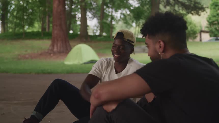 Two male friends smiling while shaking hands outside on a summer day