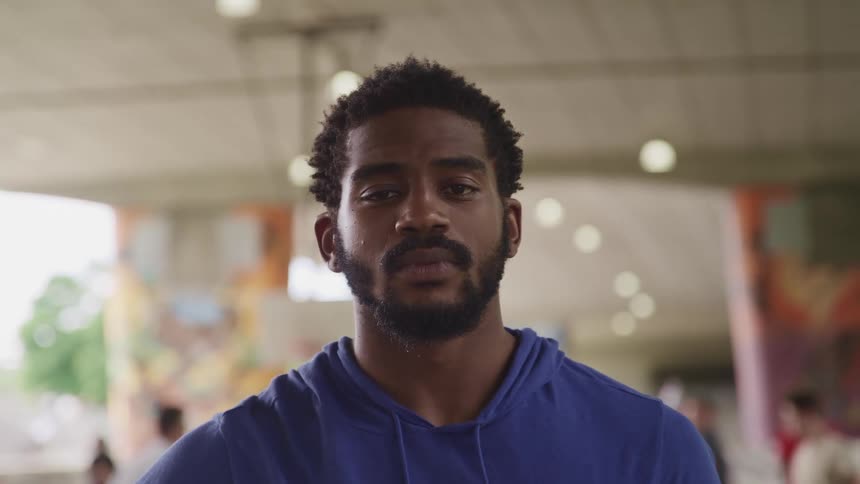 Man with a beard and a blue hoodie looks at the camera and basketball players play basketball in the background