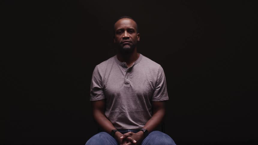 A man looking up while sitting for a portrait in front of a black background