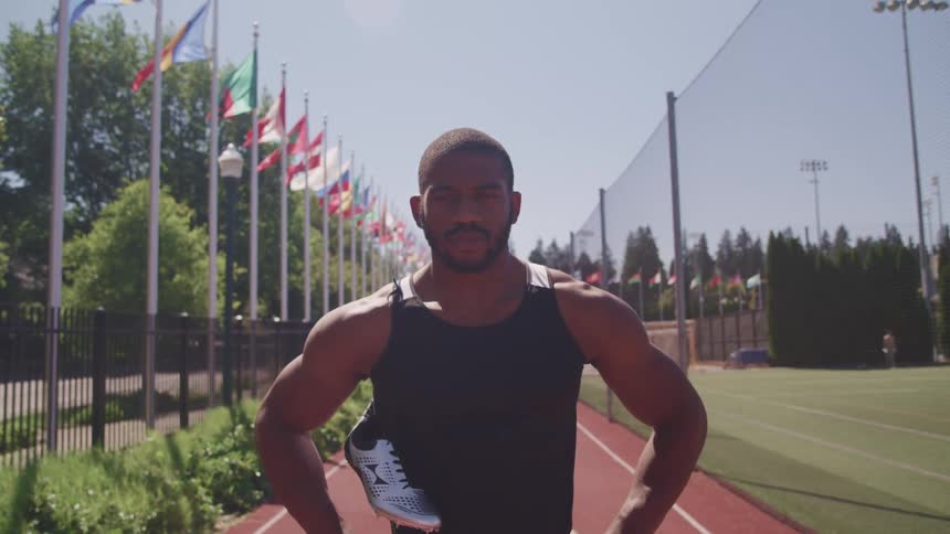 A man standing on a running track with flags trees the sky and clouds in the background