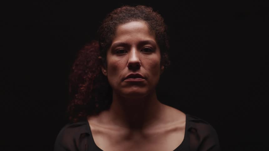 Woman sitting in a dark room looks up at the camera