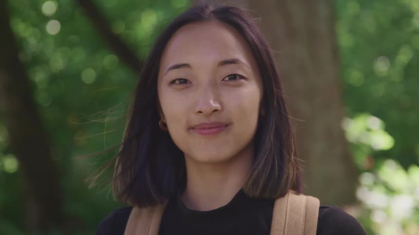 A young asian woman turns her head to look into the camera while standing outdoors on a windy day