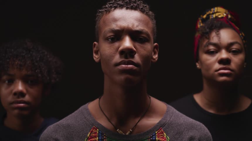 Three teenagers stand together with their heads facing away and all look forward at the same time