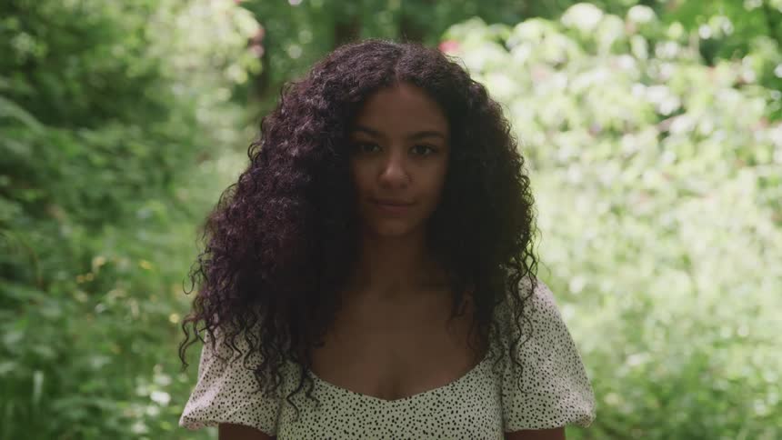 Woman with long curly hair standing in the forest looking at the cmera