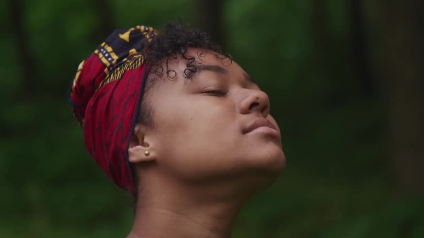 Young woman wearing a red head wrap standing in the forest looking up