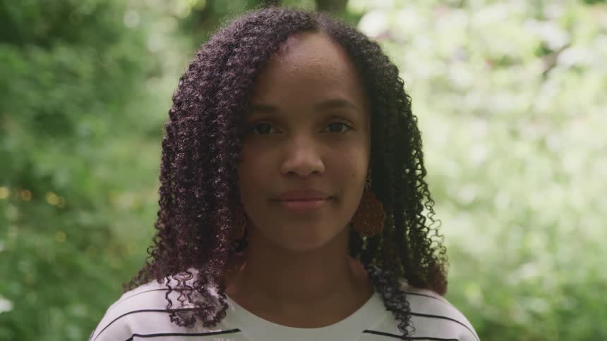 A woman with curly hair smiling for a portrait outside