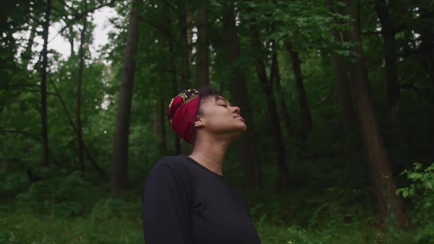 A woman closes her eyes as she stands in a forest