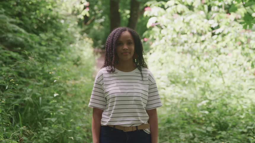 Young woman standing in the forest looking at the cmera