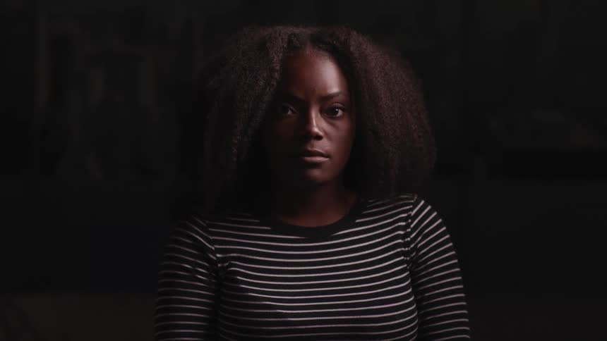Young woman standing in a dimly lit room looks up at the camera