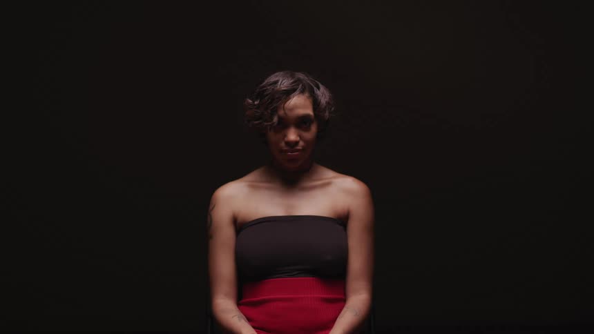 Woman sitting in a dark room looks up at the camera