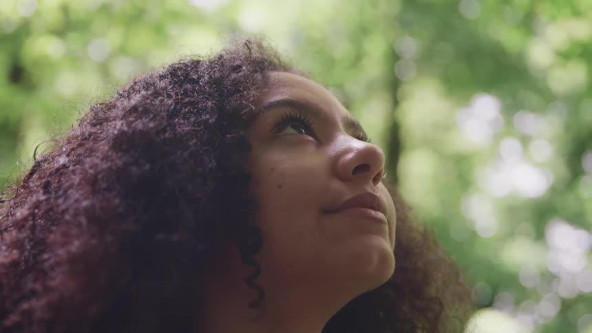 A woman with a nose ring looking off into the distance with trees the sky and clouds in the background