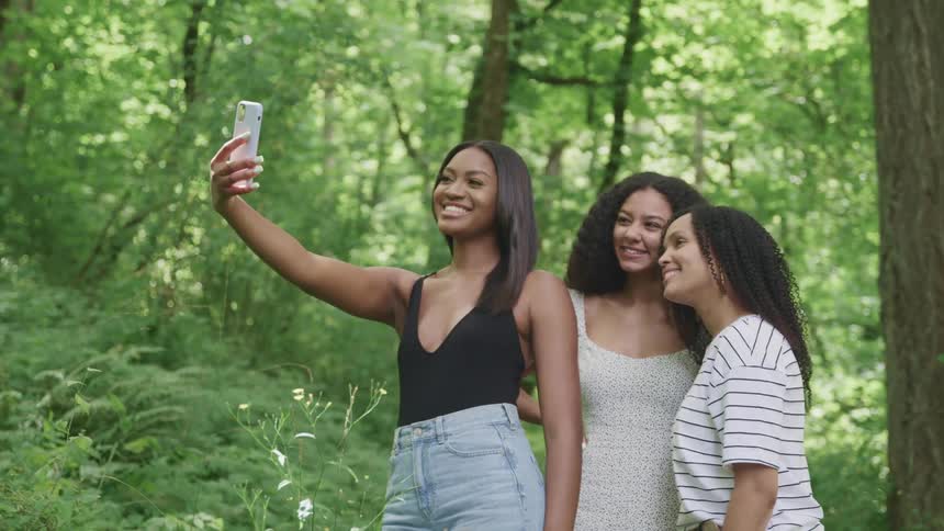 Friends stand in forest taking group photo with mobile phone
