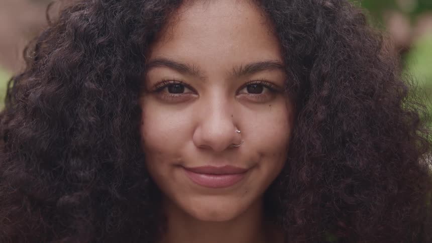 A woman with a nose ring staring with leaves in the background