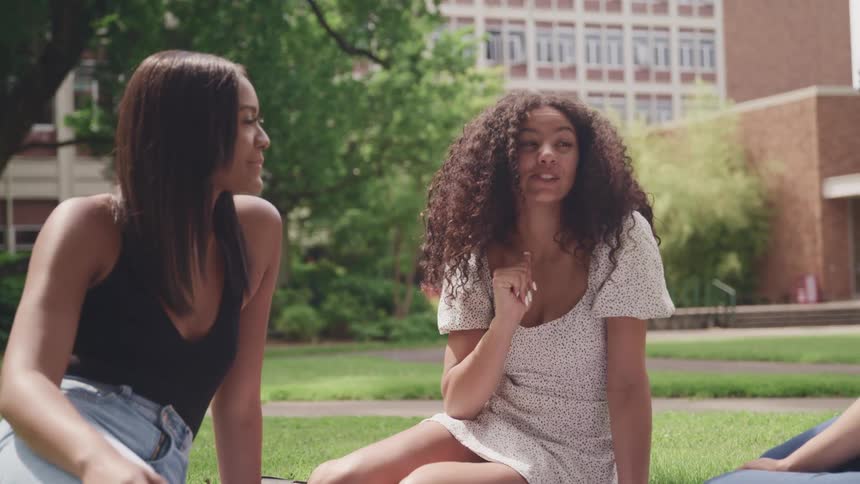 Three teenagers sit outside their school and laugh and talk