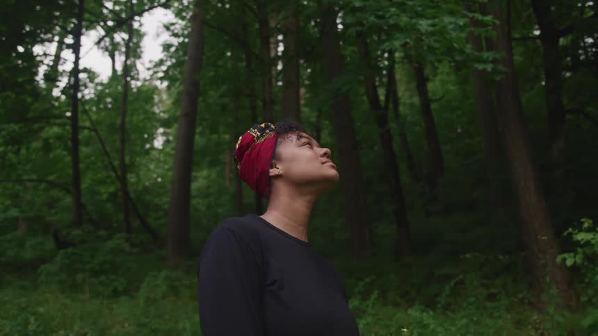 Woman wearing a red head wrap looking up in the forest