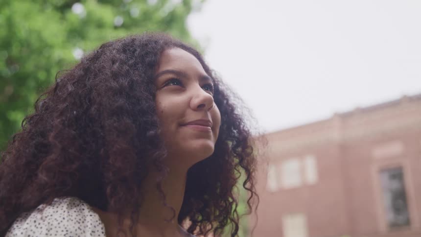 A young woman looks up at the sky while standing outdoors during the day