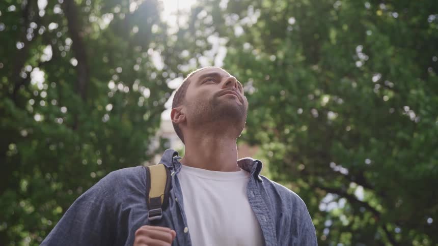 Young man carrying a backpack looks up at daytime