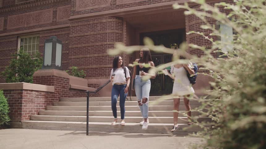 Three women leave school building smiling and talking