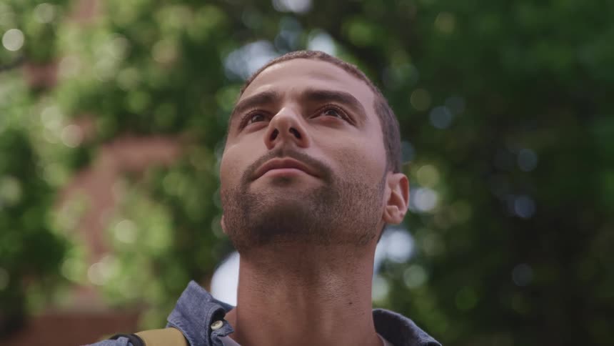 Man with slight beard stands outdoors looking up