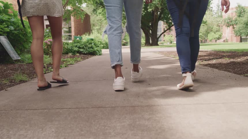 Waist down shot of three people walking on sidewalk on college campus