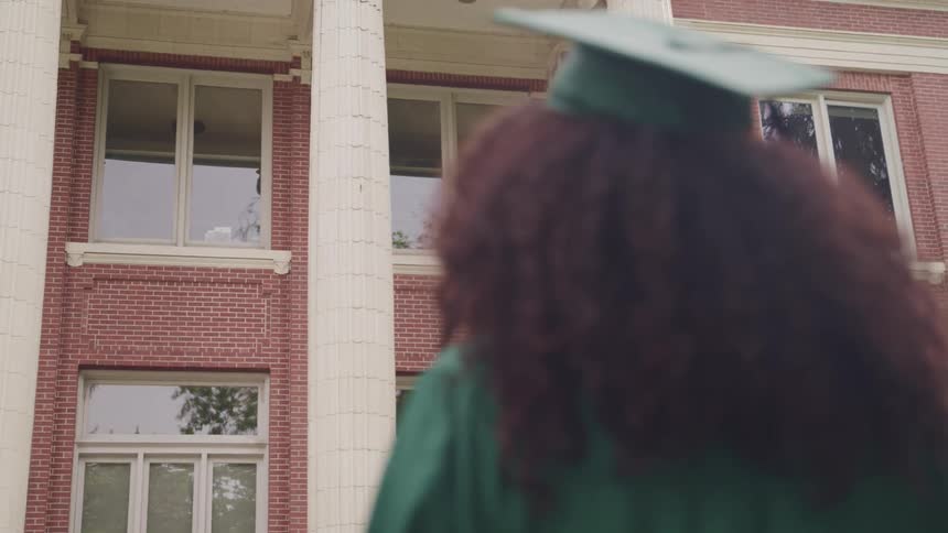 Woman with curly hari wearing graduation academic regalia in front of a building