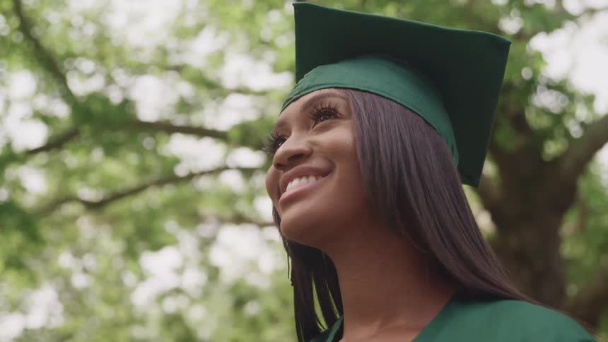A woman with a graduation cap and gown with trees the sky and clouds in the background