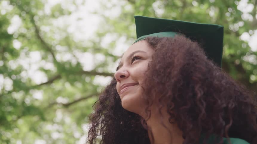 A smiling female college graduate smiling under a large tree